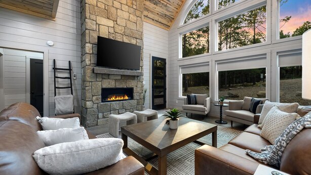 Una sala de estar acogedora con chimenea de piedra, sofás de cuero y ventanas amplias con vistas al exterior.
