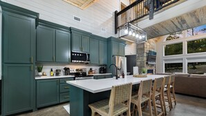 Una cocina con gabinetes color turquesa, una isla grande y una zona de comedor con sillas de madera.