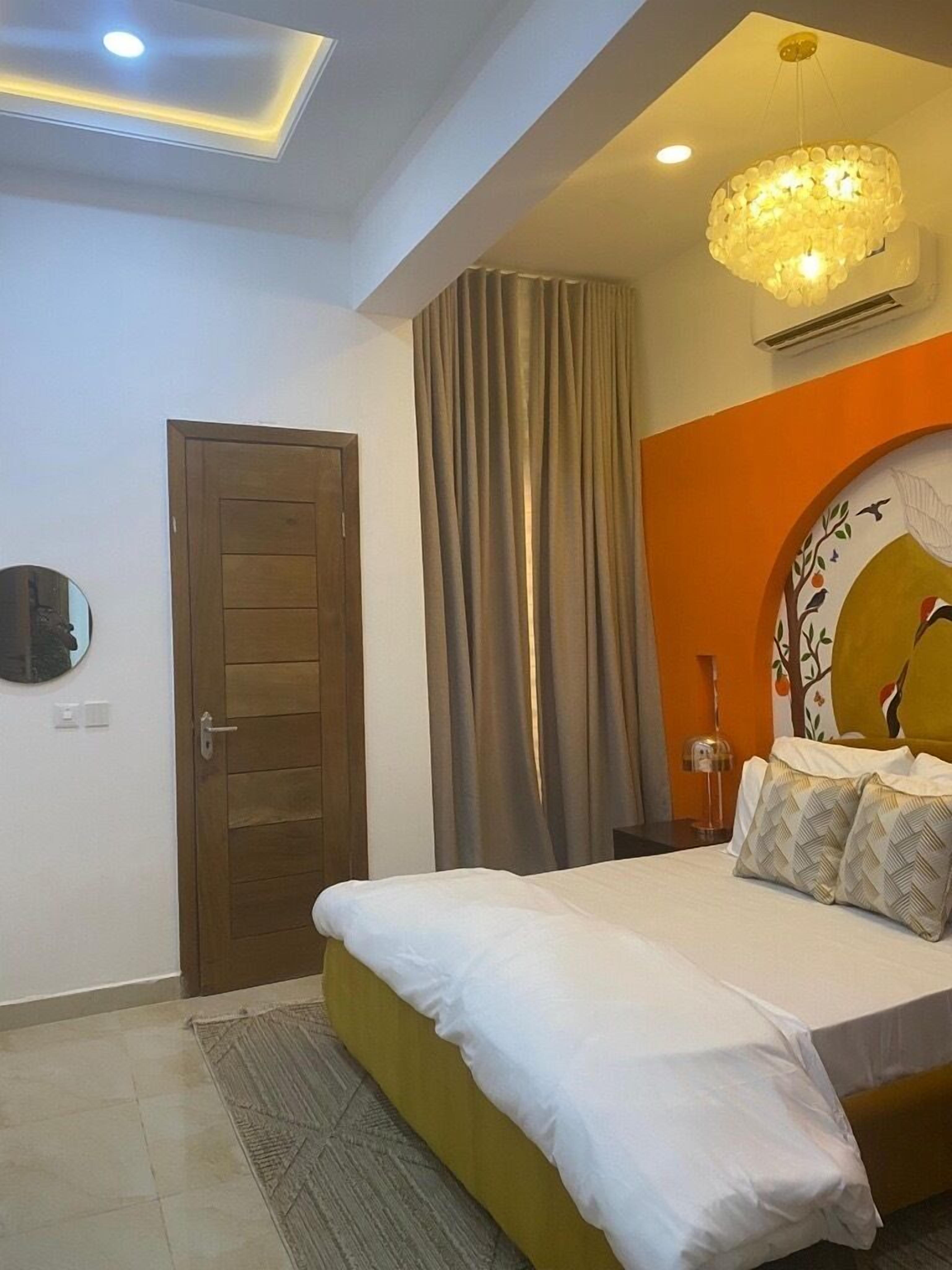 A bedroom with a bed, a wooden door, a mirror, a chandelier, and a wall with a decorative plate.