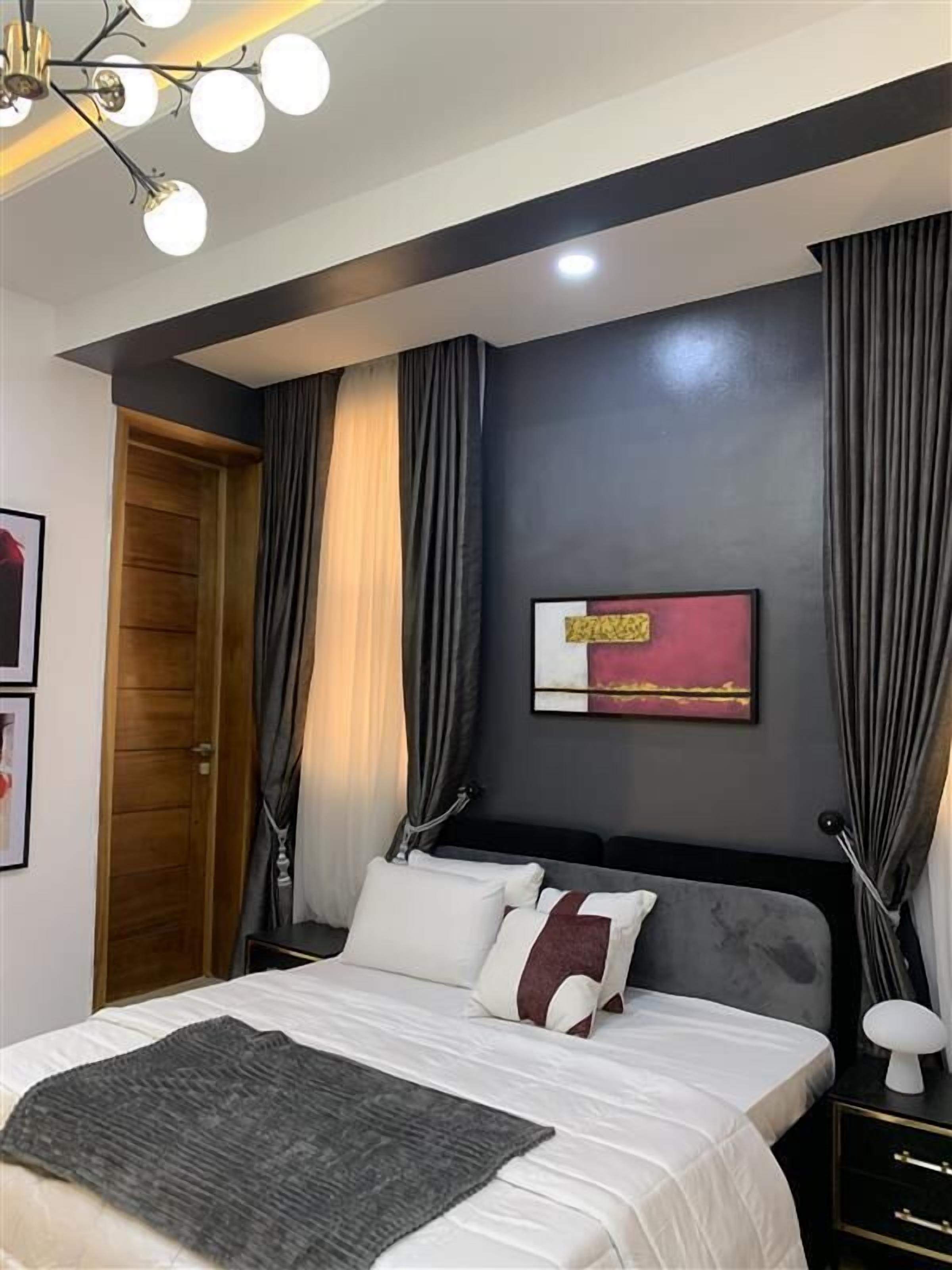 Een moderne slaapkamer met een groot bed, donkere wanden en een plafondlamp.