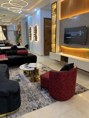 Una sala de estar moderna con un televisor de pantalla plana grande montado en la pared, un sofá negro, un sillón rojo y una mesa de centro redonda.