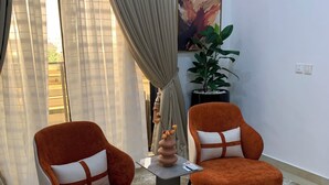 A room with two orange armchairs, a small table with a vase, and a potted plant. - Spacious 2-bedroom apartment (Lekki)