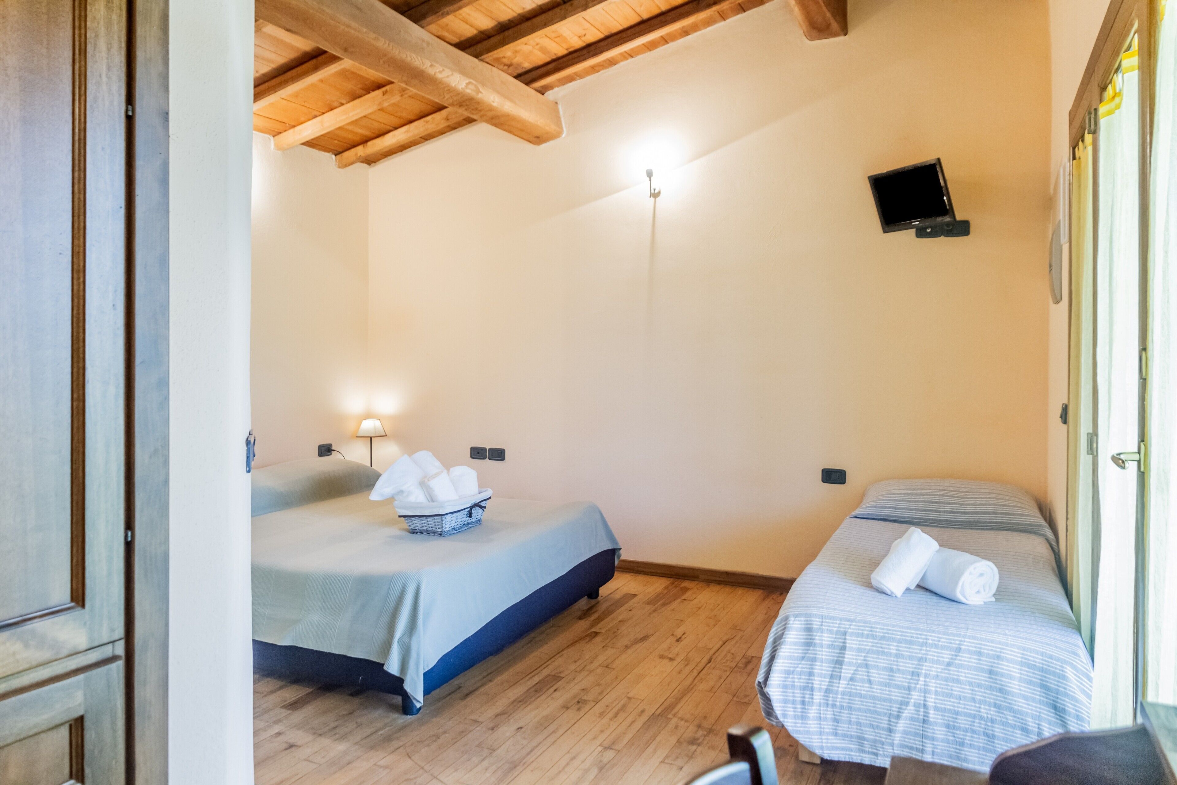 A room with two beds, a television on the wall, and a wooden ceiling.
