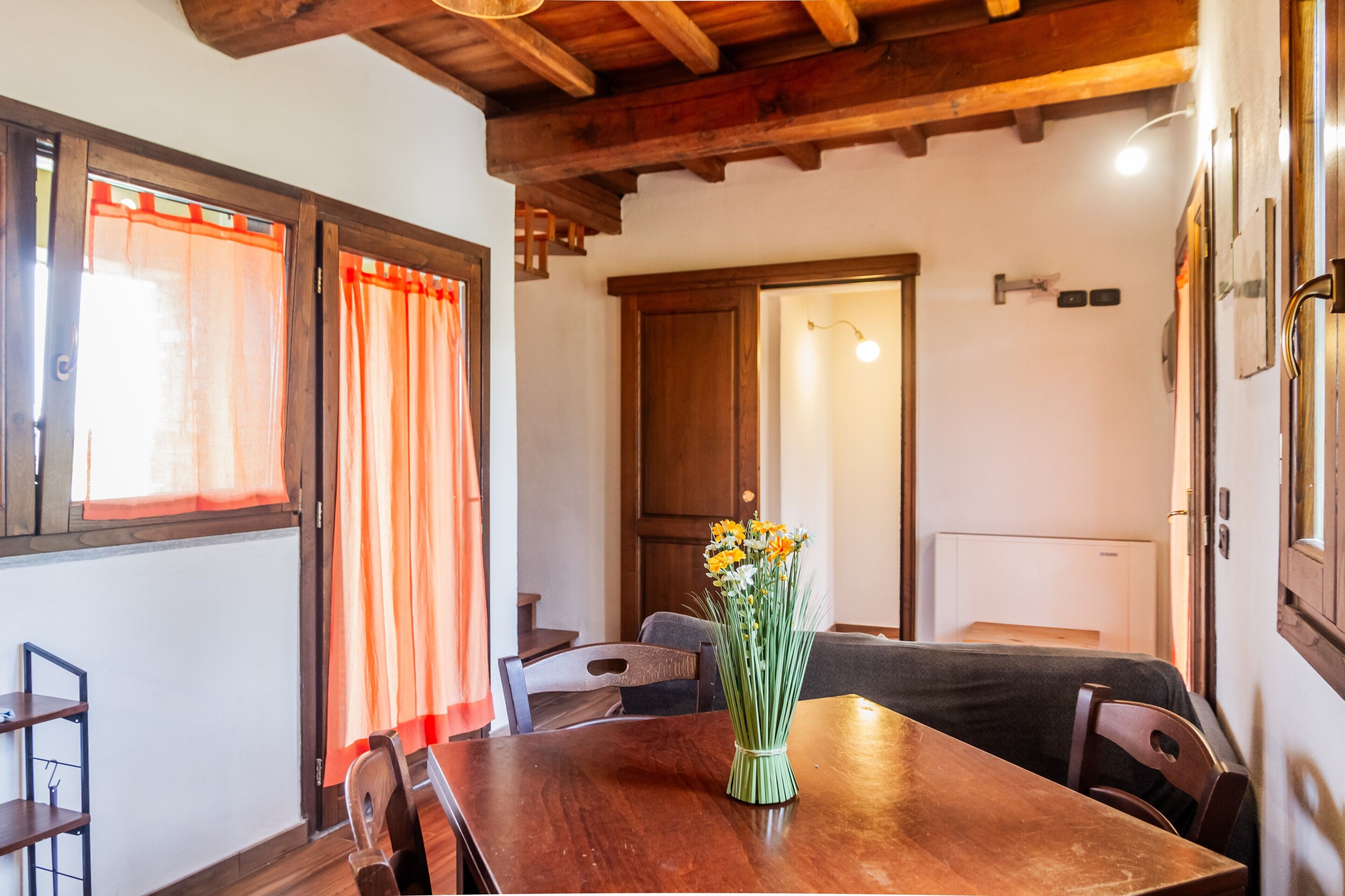 A dining area with a wooden table, chairs, a vase with flowers, and a wooden ceiling.