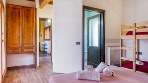 A room with a bunk bed, wooden wardrobe, and a door leading to another room.