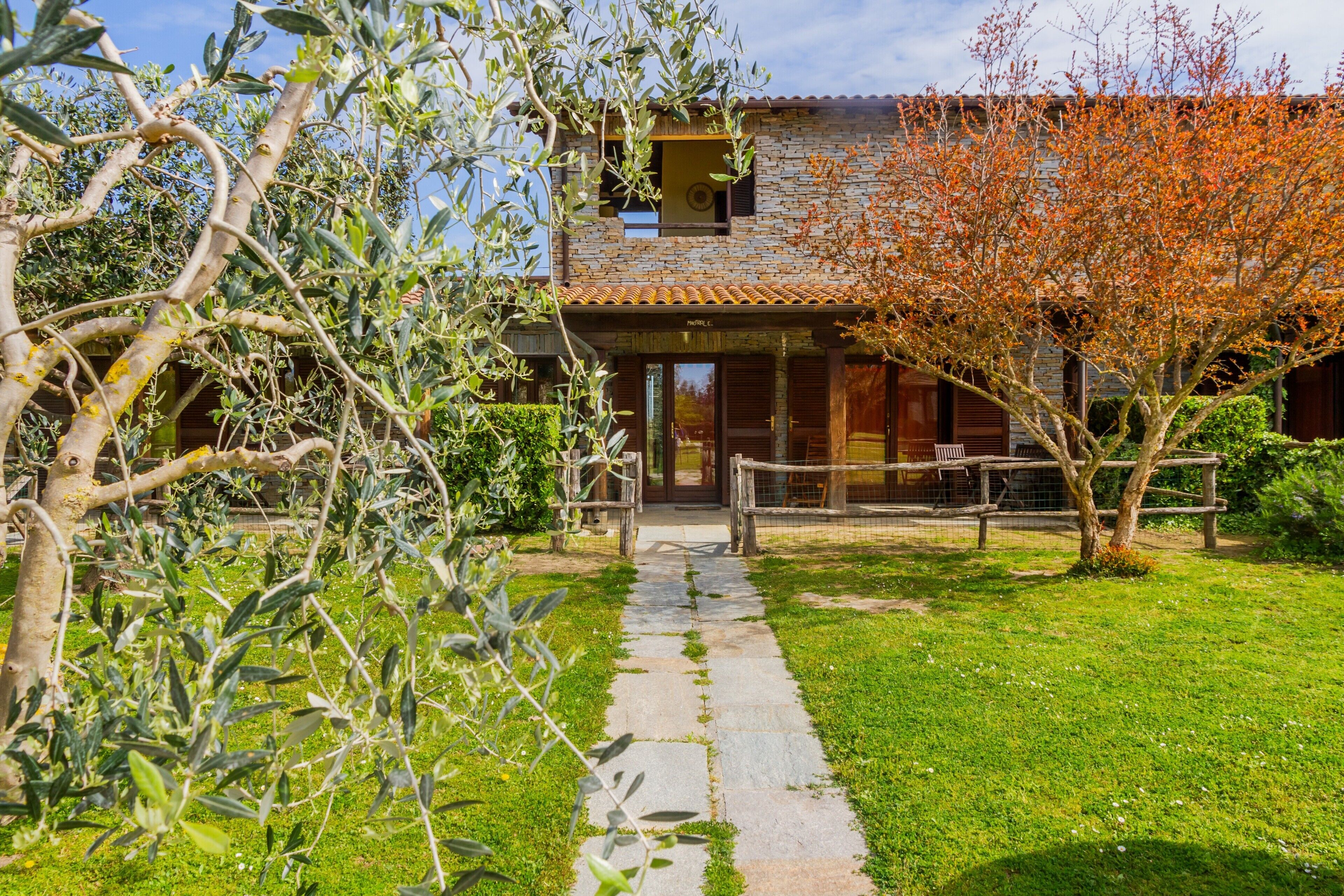 A stone pathway leading to a rustic building with a tiled roof and wooden shutters.