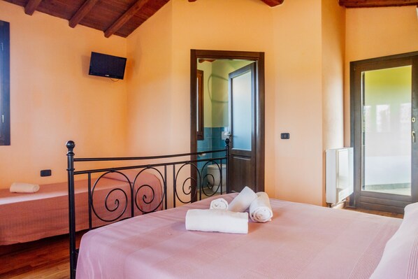 A bedroom with a bed, a TV mounted on the wall, and a door leading to a balcony.