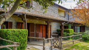 A rustic stone building with a wooden porch, a fenced garden, and a clear sky.