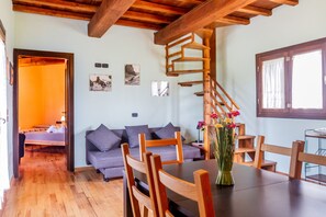 A room with a wooden staircase, a sofa, a dining table with chairs, and a vase of flowers.