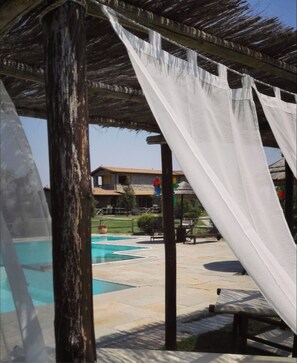 A pool area with a pergola structure, a clear sky, and a building in the background.