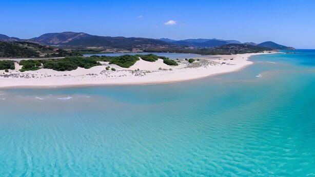 Un paisaje costero con una playa arenosa, aguas turquesas cristalinas y montañas distantes.