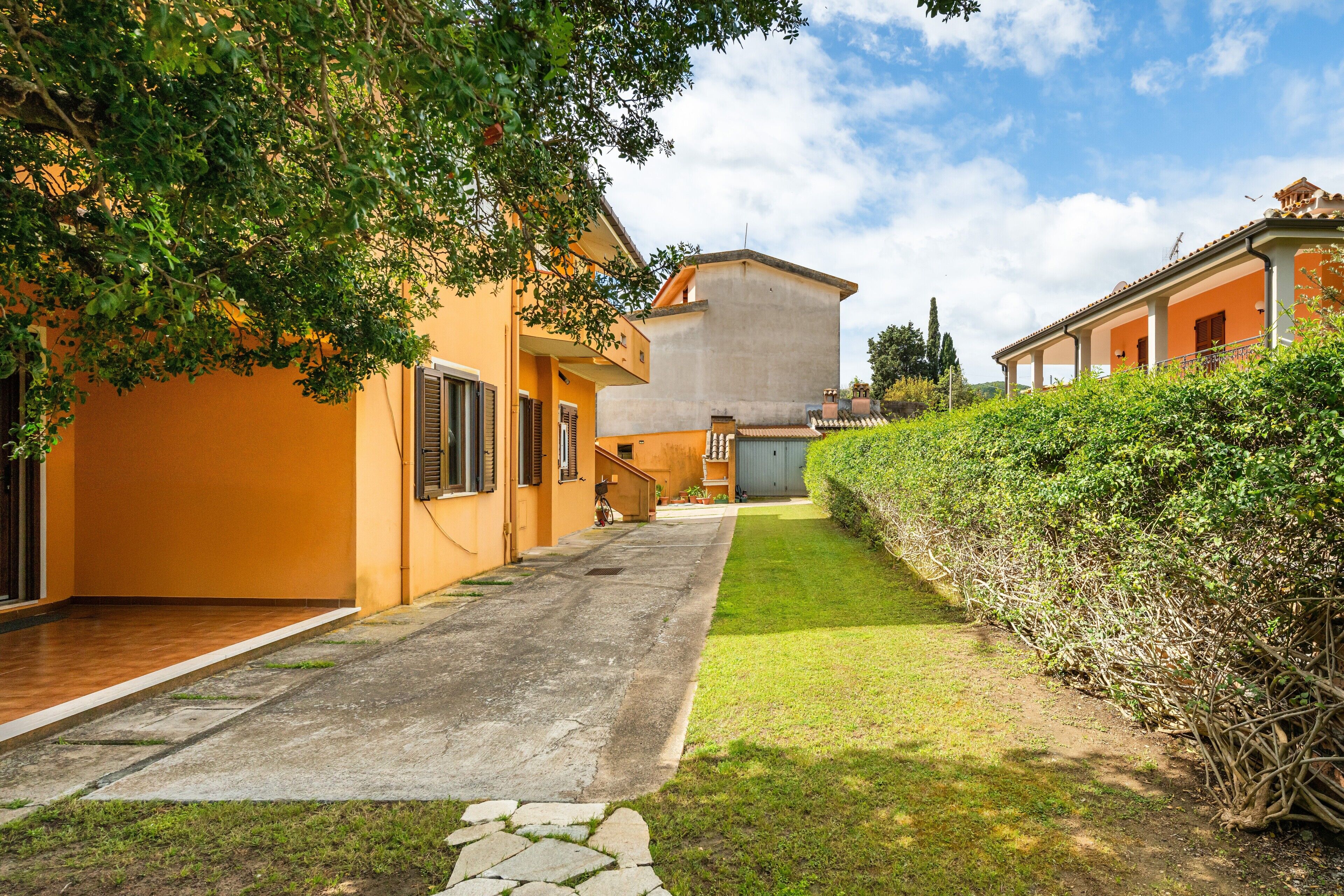A residential property with a paved driveway, a well-maintained lawn, and a hedge along the right side.