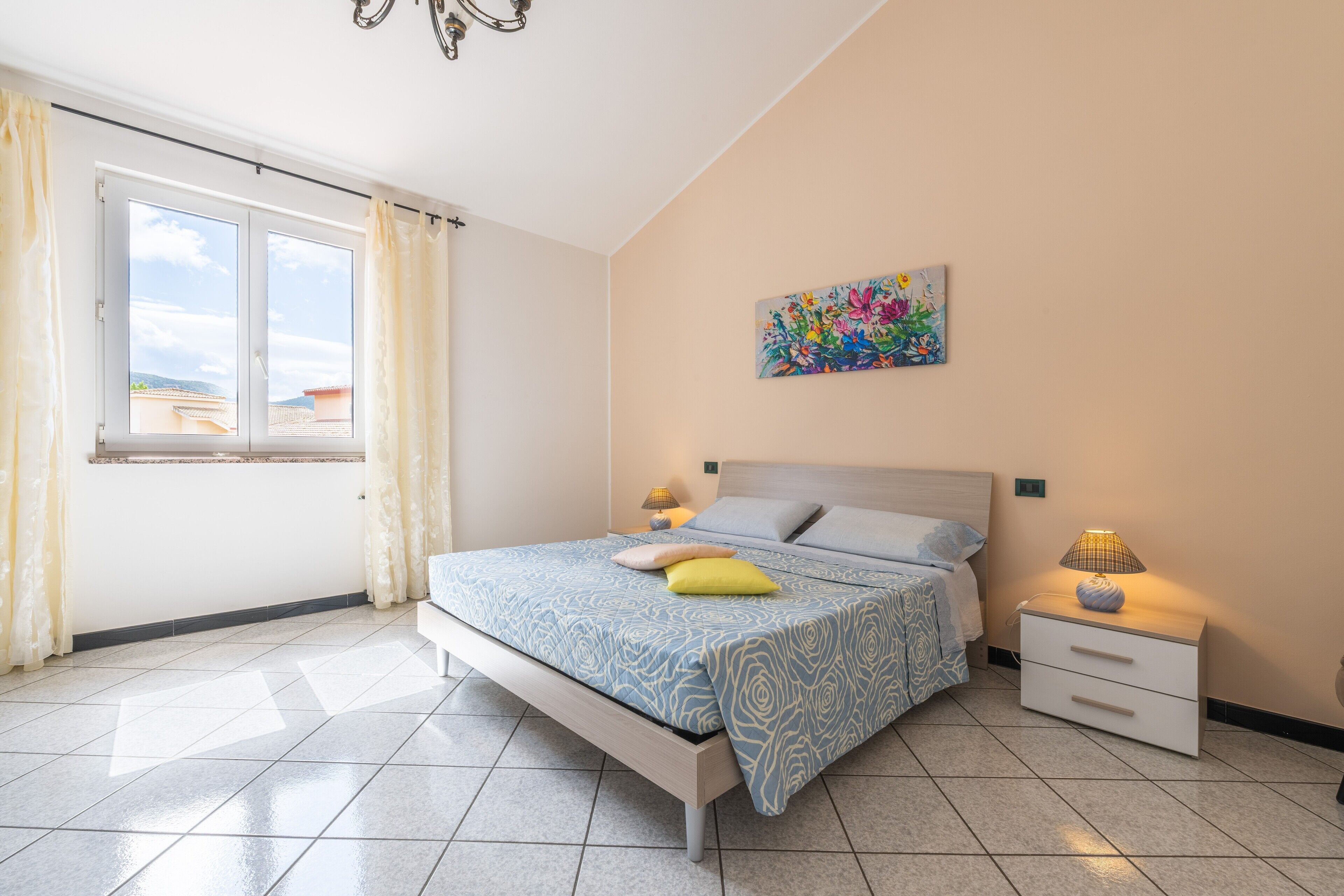Une chambre à coucher avec un lit, des tables de chevet, une fenêtre et un tableau au mur.