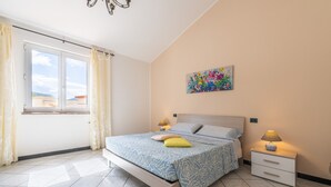 Un dormitorio con cama, mesitas de noche, una ventana y un cuadro en la pared.