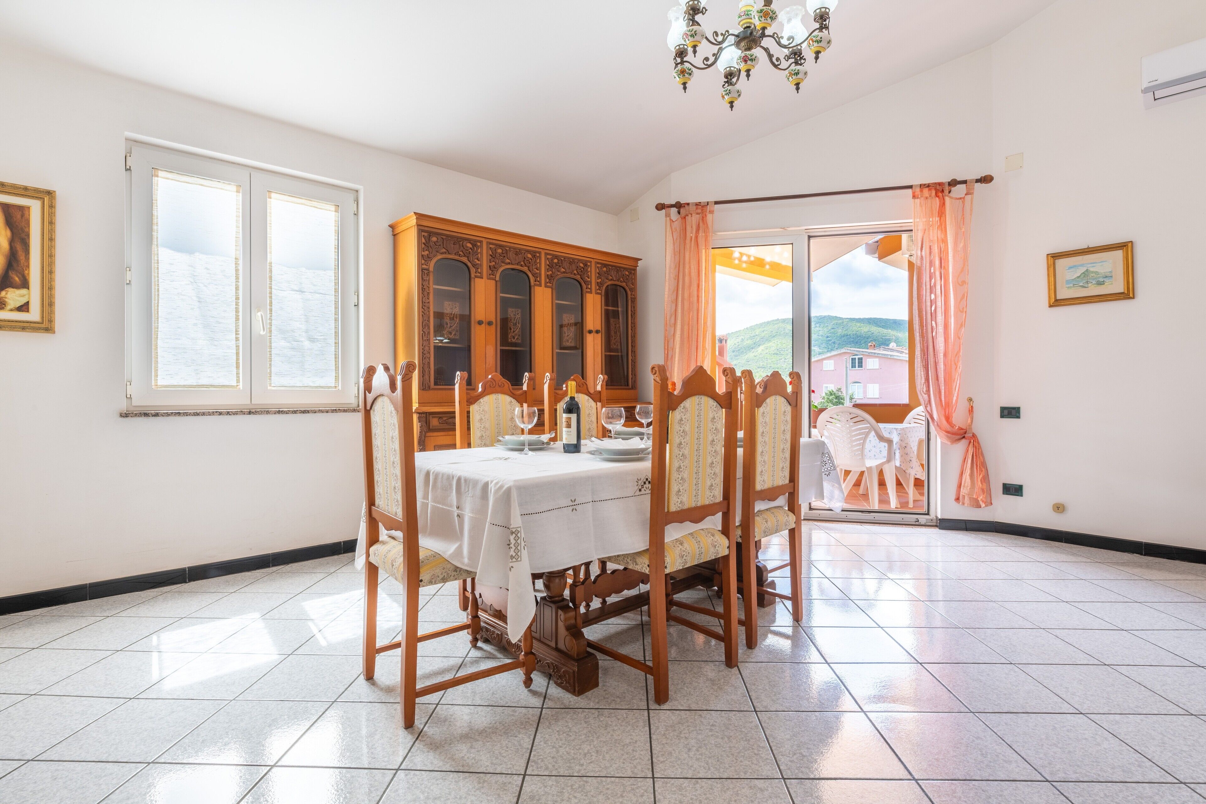 Un coin repas avec une table dressée pour quatre personnes, un buffet en bois et une vue à travers une porte vitrée.