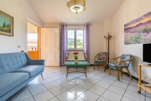 En stue med sofa, et bord med blomster, to mønstrede stole, et fjernsyn og et billede på væggen.