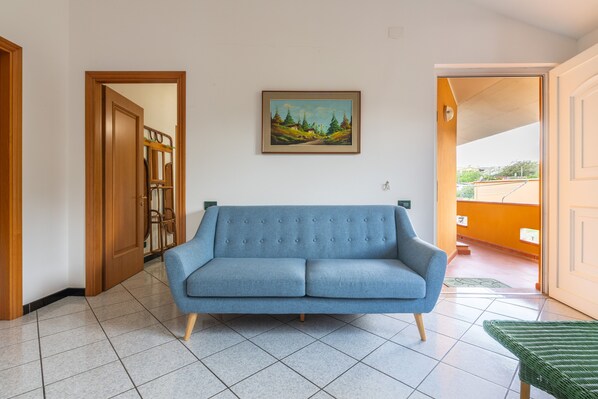 A room with a blue sofa, a painting on the wall, and a door leading to another room.