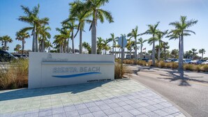 Schild für den Siesta Beach im Sarasota County, Florida, mit Palmen und einem Parkplatz im Hintergrund.