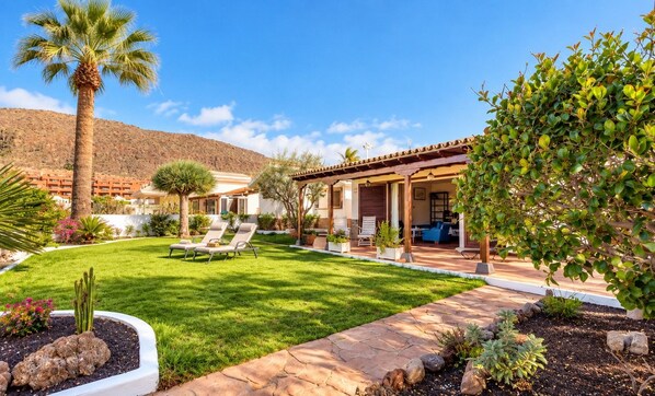 A residential property with a patio area, outdoor seating, and a well-maintained lawn.