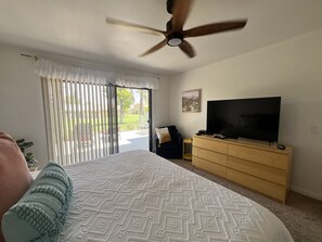 A bedroom with a bed, a ceiling fan, a TV on a wooden dresser, and a sliding glass door leading to a patio.