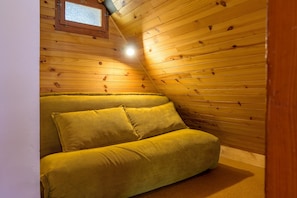 A room with wooden walls, a window, and a green sofa.