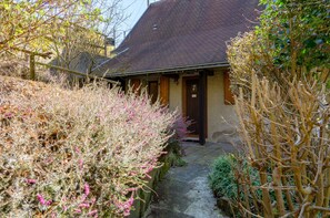 A traditional building with a sloped roof, a stone pathway leading to the entrance, and a small garden area with flowering plants.