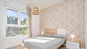 Un dormitorio con cama, mesitas de noche, una lámpara colgante, una ventana con cortinas y un papel tapiz estampado.