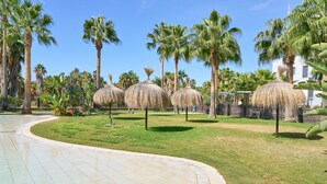 Un sendero pavimentado, palmeras y sombrillas de paja en un entorno de resort.