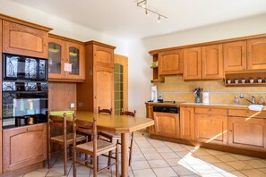 Une cuisine avec des meubles de rangement en bois, une table à manger avec des chaises, un lave-vaisselle et un four à micro-ondes.