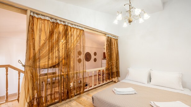 A bedroom with a bed, white pillows, a chandelier, a wooden floor, and a balcony with a railing. - Studio 'Fanes 3' with Mountain View, Wi-Fi and Air Conditioning (Rhodes)