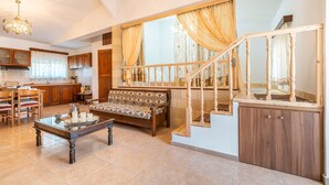 A spacious living area with a sofa, coffee table, and dining set. A staircase with a wooden railing leads to an upper level. - Studio 'Fanes 3' with Mountain View, Wi-Fi and Air Conditioning (Rhodes)