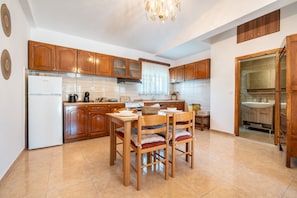 A kitchen with wooden cabinets, a white refrigerator, a dining table with chairs, and a chandelier.