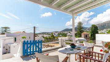 Una terraza con una mesa y sillas blancas, un portón azul y vistas a un pueblo y montañas.
