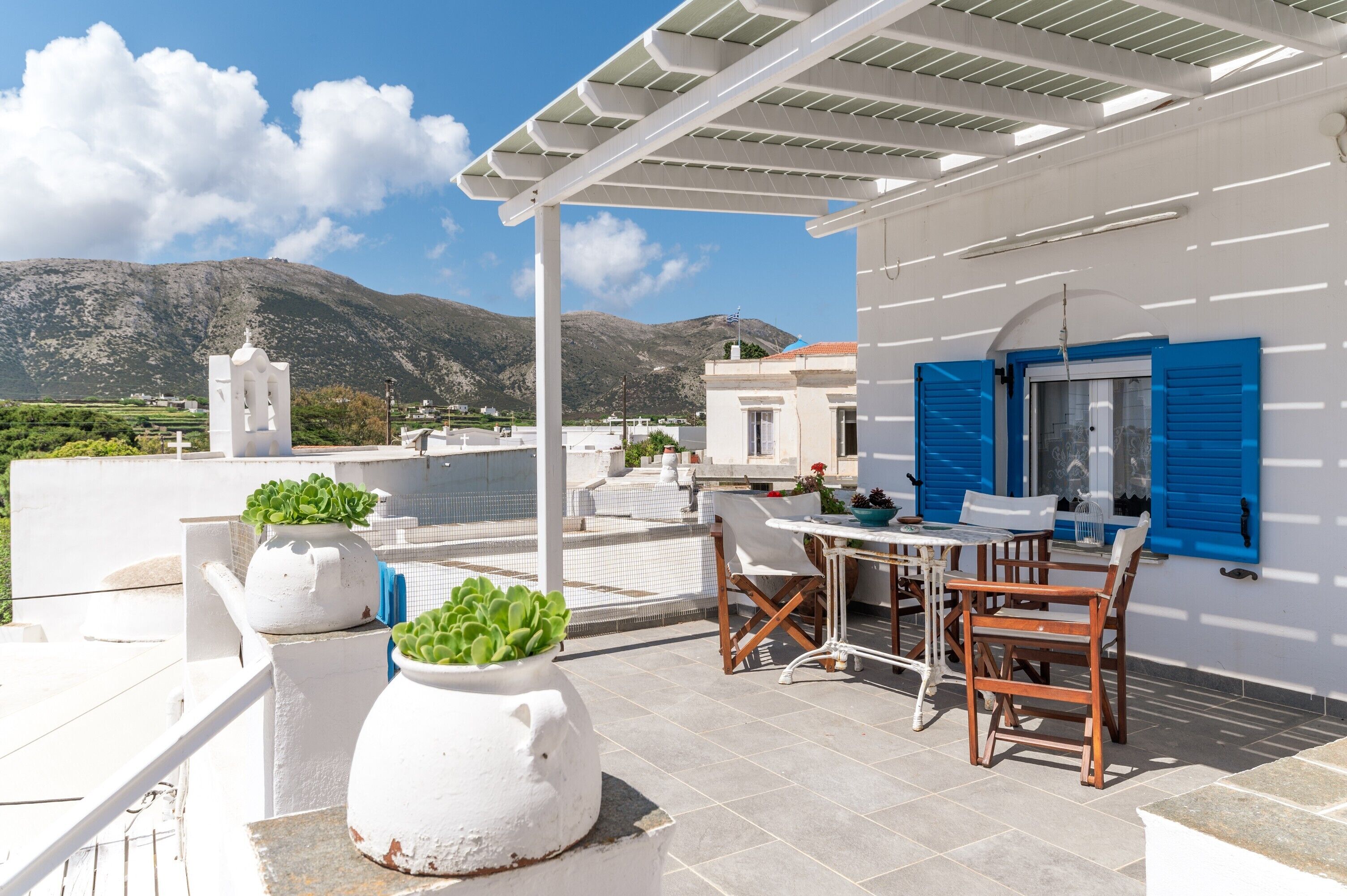 Une terrasse sur le toit, avec une table et des chaises, des plantes en pot et une vue sur les montagnes.