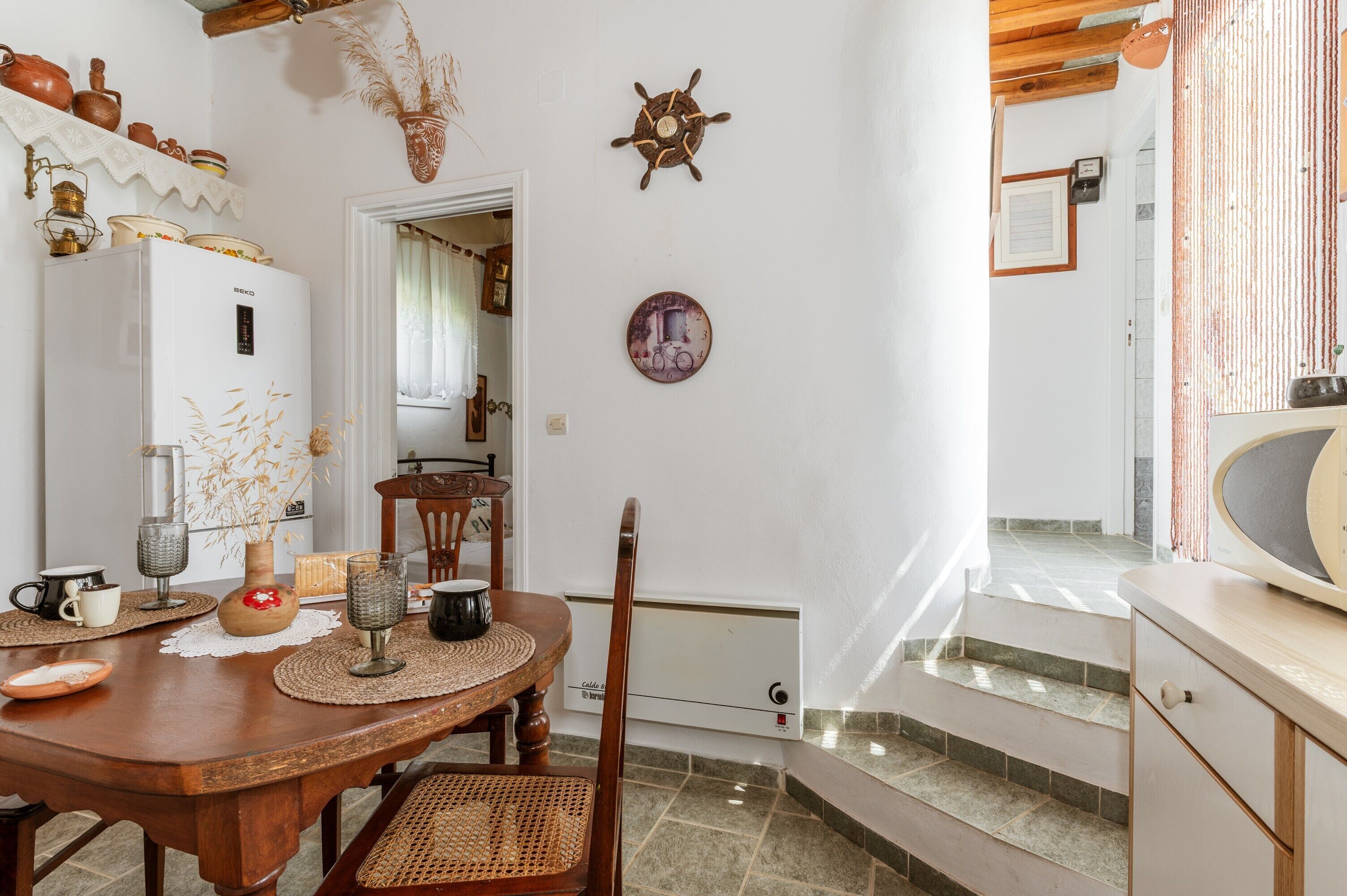 A dining area with a wooden table, chairs, a white refrigerator, and a wall-mounted clock.