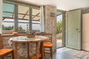 Pared de piedra, mesa de madera, sillas, una puerta y una ventana con vistas.