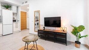 Een moderne woonkamer met een flatscreen televisie, een houten console tafel, een rieten stoel en een potplant.