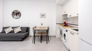 Een moderne woonruimte met een bank, eettafel, stoelen, een klok, een lijst met een afbeelding, een wasmachine en een keukenhoek.
