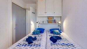 Un dormitorio con dos camas, un armario, una estantería con libros y una lámpara, y una lámpara colgante.