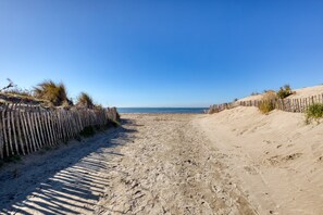 Ein sandiger Strandweg mit Holzzäunen an beiden Seiten, der zum Meer führt.