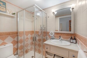 Un baño con cabina de ducha de vidrio, un lavabo con espejo y un inodoro.