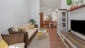 A living room with a sofa, a small table with a plant, a TV, and a kitchen area in the background. - Holiday Apartment 'Casa Eusebia' with Wi-Fi (Arona)