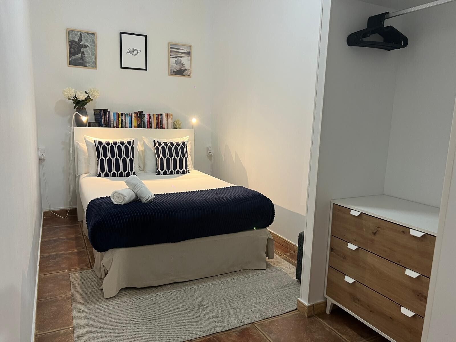 A neatly arranged bedroom with a bed, bedside tables, a dresser, and wall art.