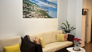A living room with a large wall-mounted picture, a brown wicker sofa, a beige sofa, and a small white table with a vase of red flowers. - Holiday Apartment 'Casa Eusebia' with Wi-Fi (Arona)