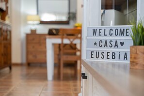 Un letrero con la palabra 'WELCOME' y 'CASA', ubicado en un pasillo con piso de madera y muebles.