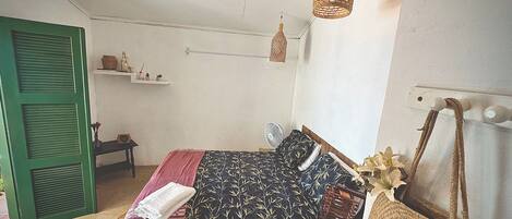 A bedroom with a bed, a bedside table, a hanging light, and a green door.