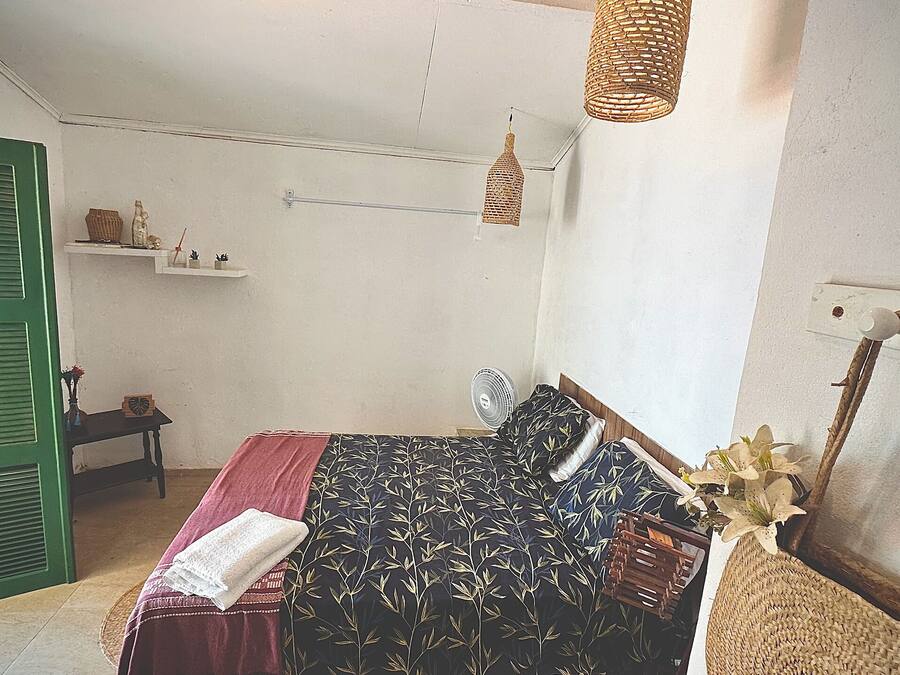 Quarto com cama, mesa de cabeceira, luminária pendente e porta verde.