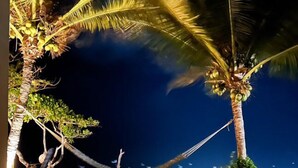 A room with a view of a beach at night, featuring palm trees and a hammock. - Pousada Vila Matury (Icapuí)