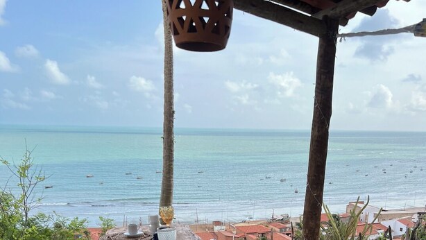 An outdoor dining area with a view of the sea and buildings in the background. - Pousada Vila Matury (Icapuí)