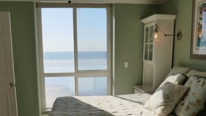 A bedroom with a bed, a ceiling fan, a view of the beach, and a door leading to the beach. - Tranquil 2 Bd Oceanfront Condo in charming Oceanside with WiFi, fitness room. (Oceanside)